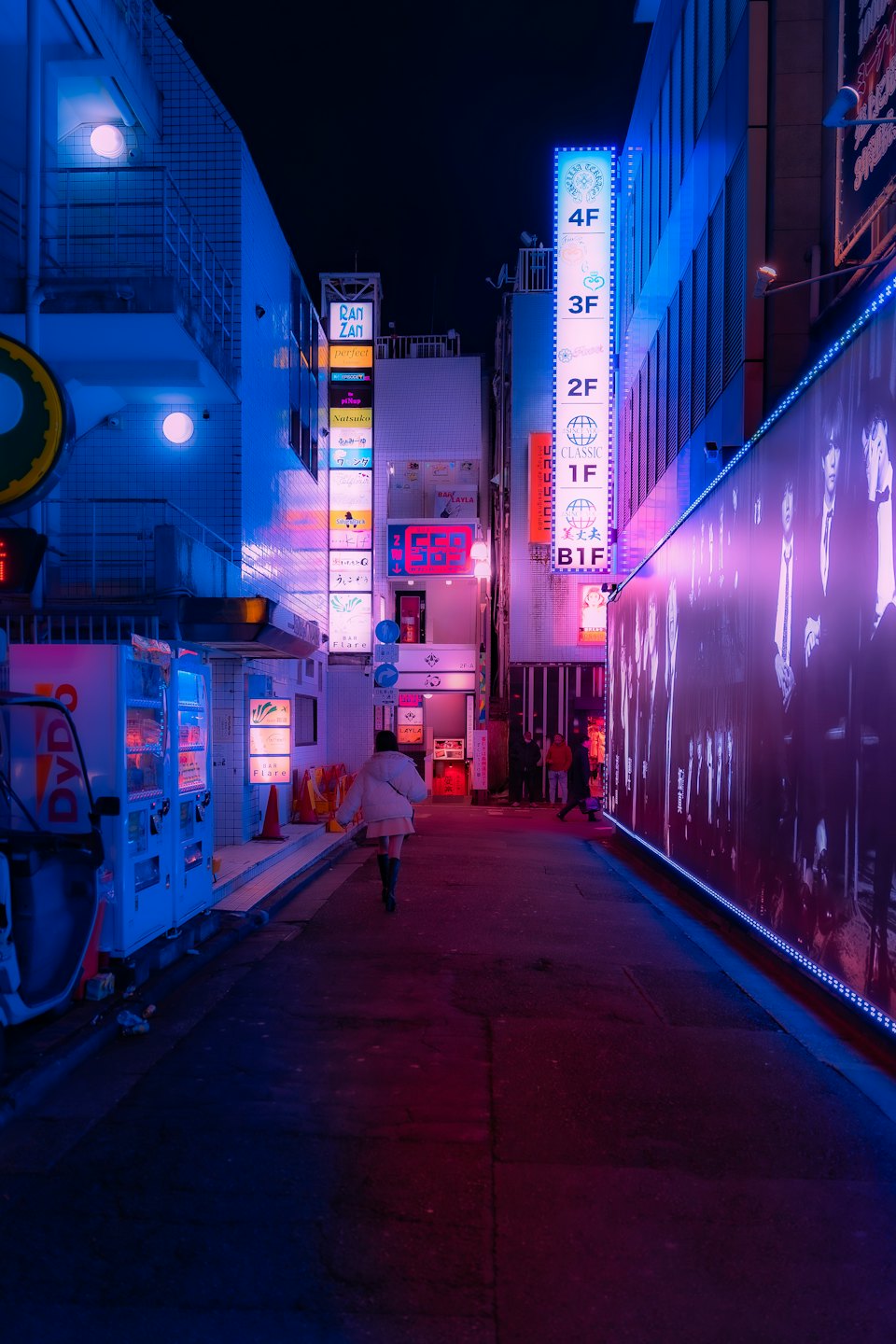 Person walks down neon-lit alley with Japanese signs.