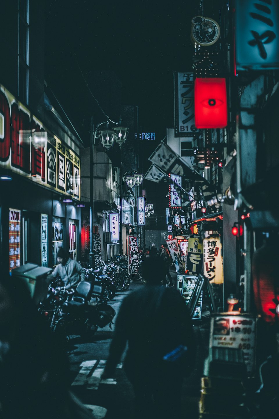 People walk through a narrow urban alley filled with neon signs.